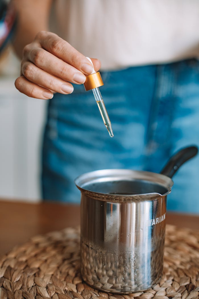 Hand with dropper adding liquid to coffee in a silver mug for flavoring or testing.