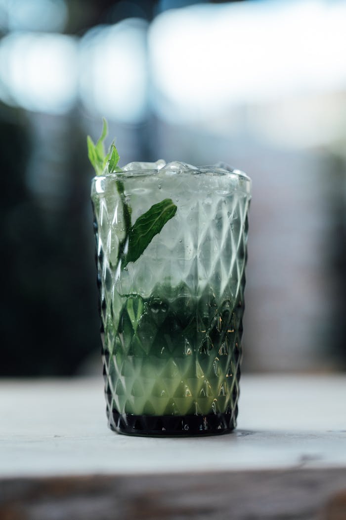 Close-up shot of a mojito cocktail in a textured glass with fresh mint leaves.